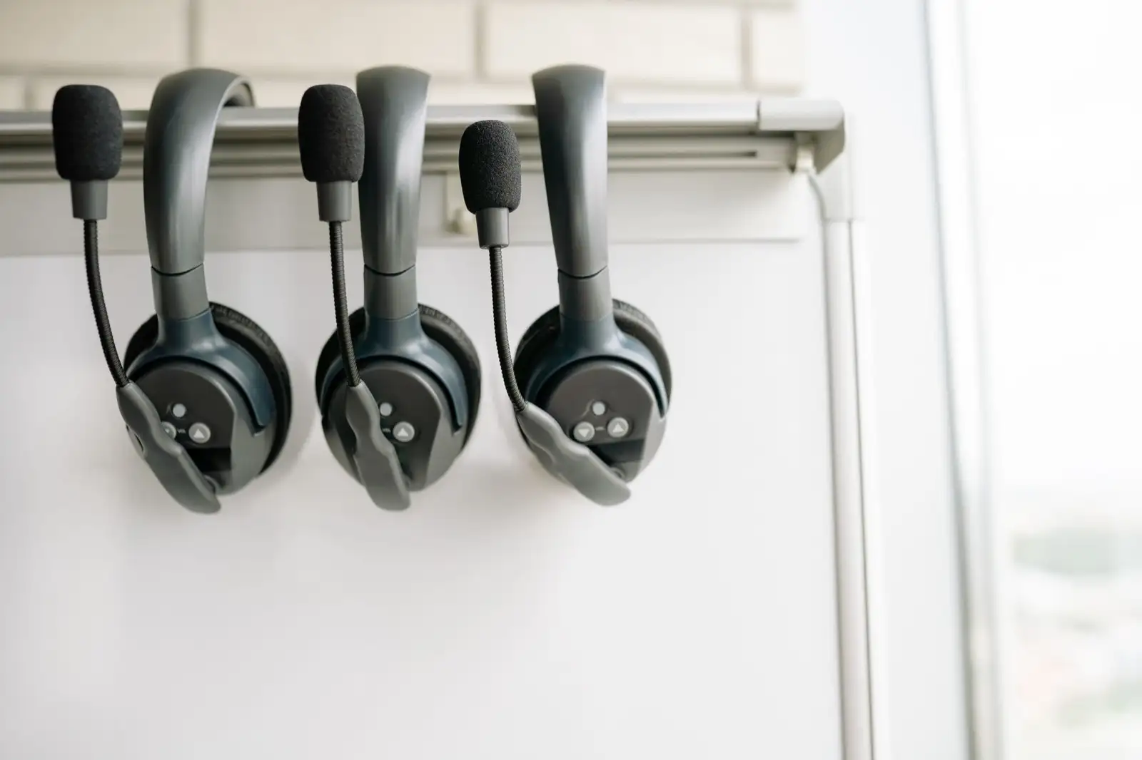 Three headsets with microphones hanging from a rail