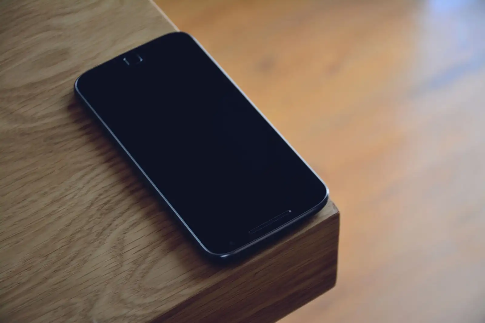 Smartphone with a dark screen resting on the corner of a wooden table