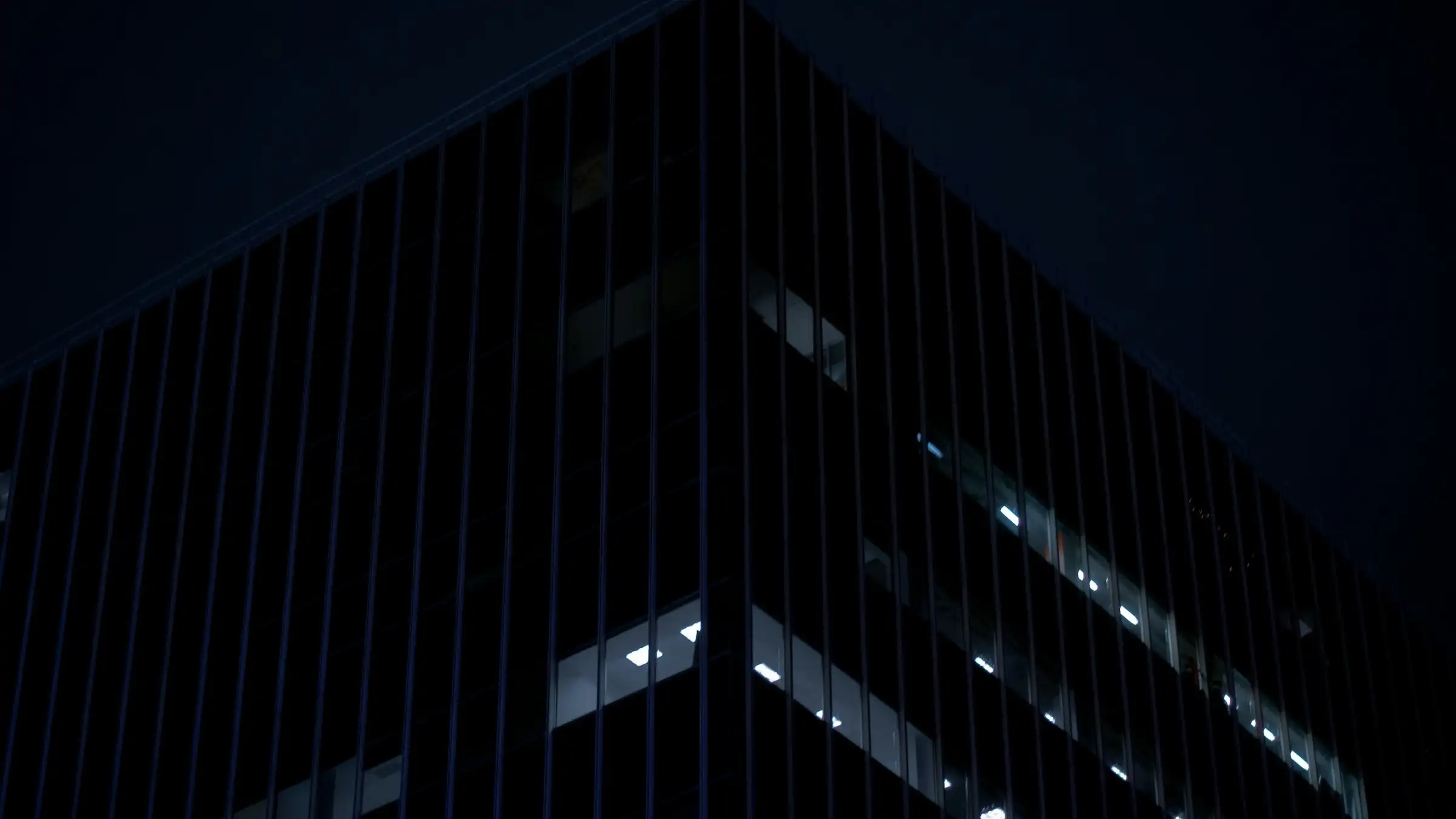Dark glass office building at dusk with a few lit windows