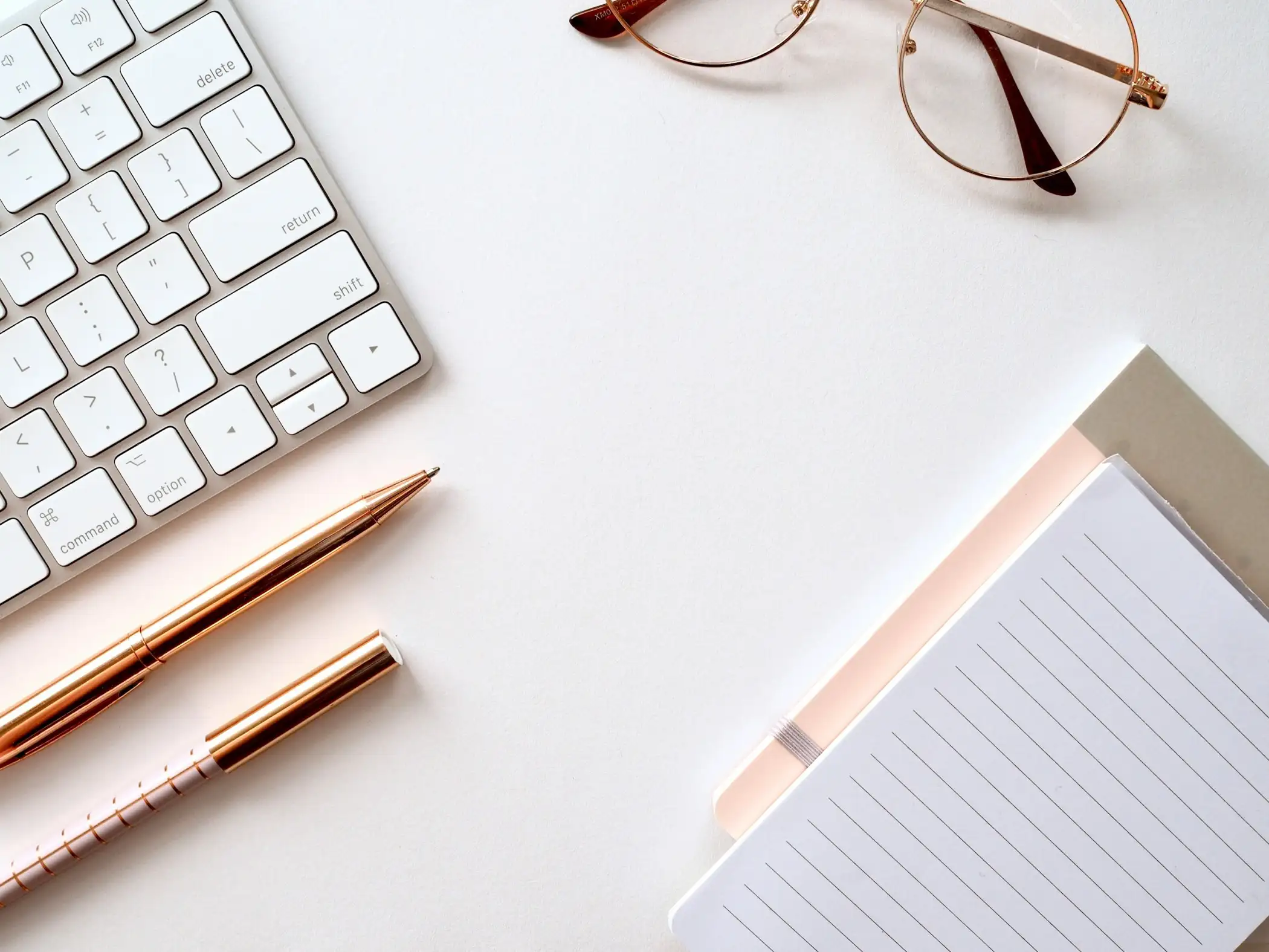 Keyboard, pen, glasses and a lined notepad on a white desk