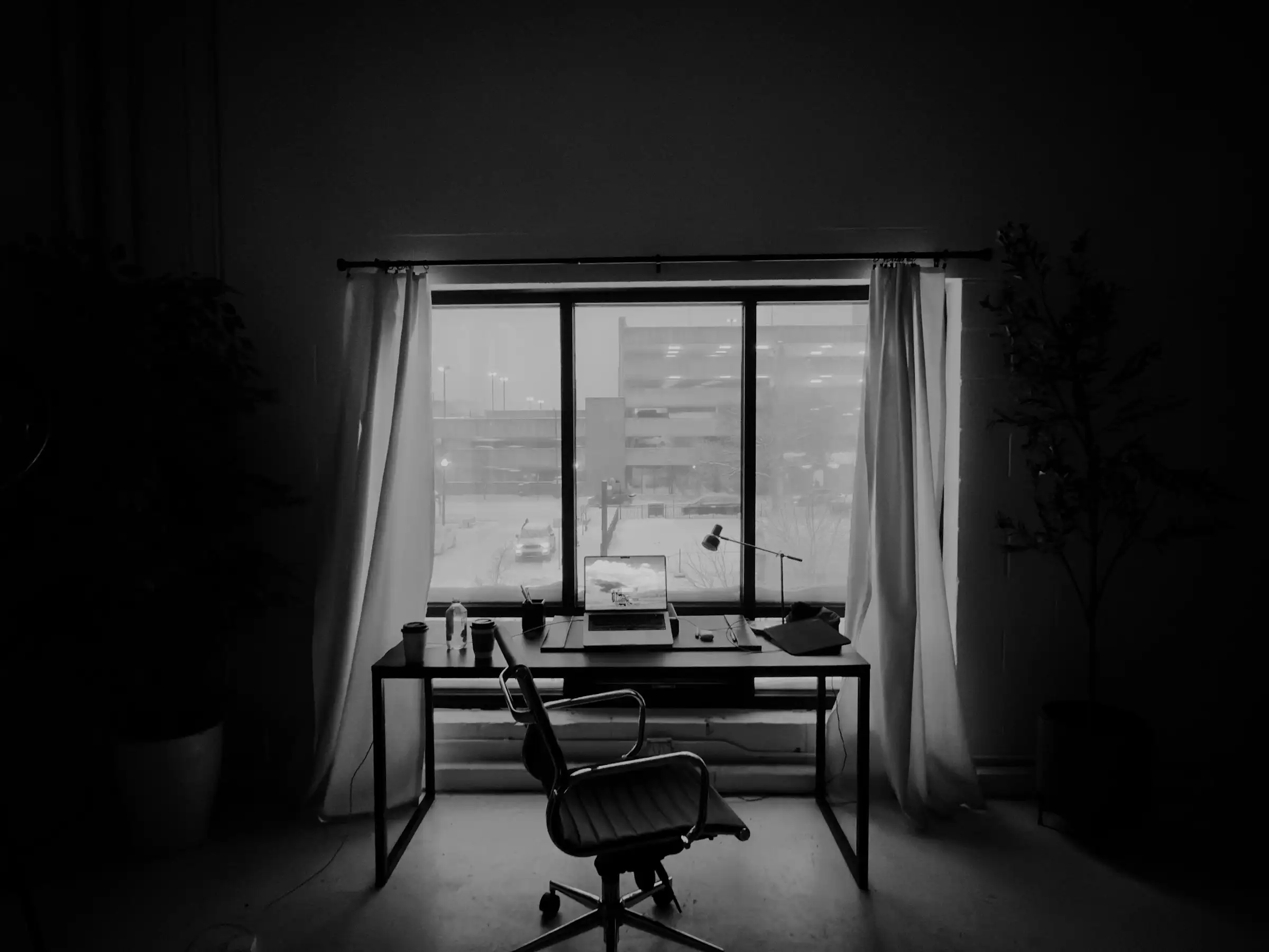 Empty desk and office chair in front of a window in a dim room